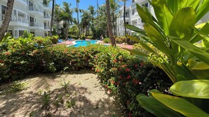 Zwembadgedeelte van een resort met palmbomen, een helderblauwe lucht en een gebouw met balkons.