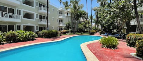 Ein Pool mit roter Einfassung, umgeben von Palmen und einem mehrstöckigen Gebäude mit Balkonen.