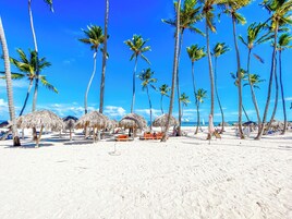 Una playa con palmeras y sombrillas de paja.