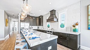 A modern kitchen with a large island, dark cabinetry, and a white backsplash. - Amazing home on canal! Paddle boards, and kayaks! (Bradenton Beach)