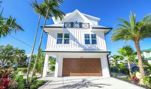 A two-story house with a garage, surrounded by palm trees and a clear sky. - Amazing home on canal! Paddle boards, and kayaks! (Bradenton Beach)