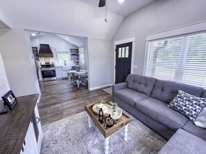En moderne stue med en grå sofa, et træbord og et spiseområde i baggrunden.