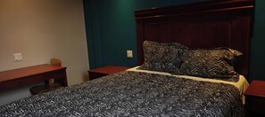 A bedroom with a bed, a nightstand, a dresser, and a desk. - Queensway Motel (Toronto)
