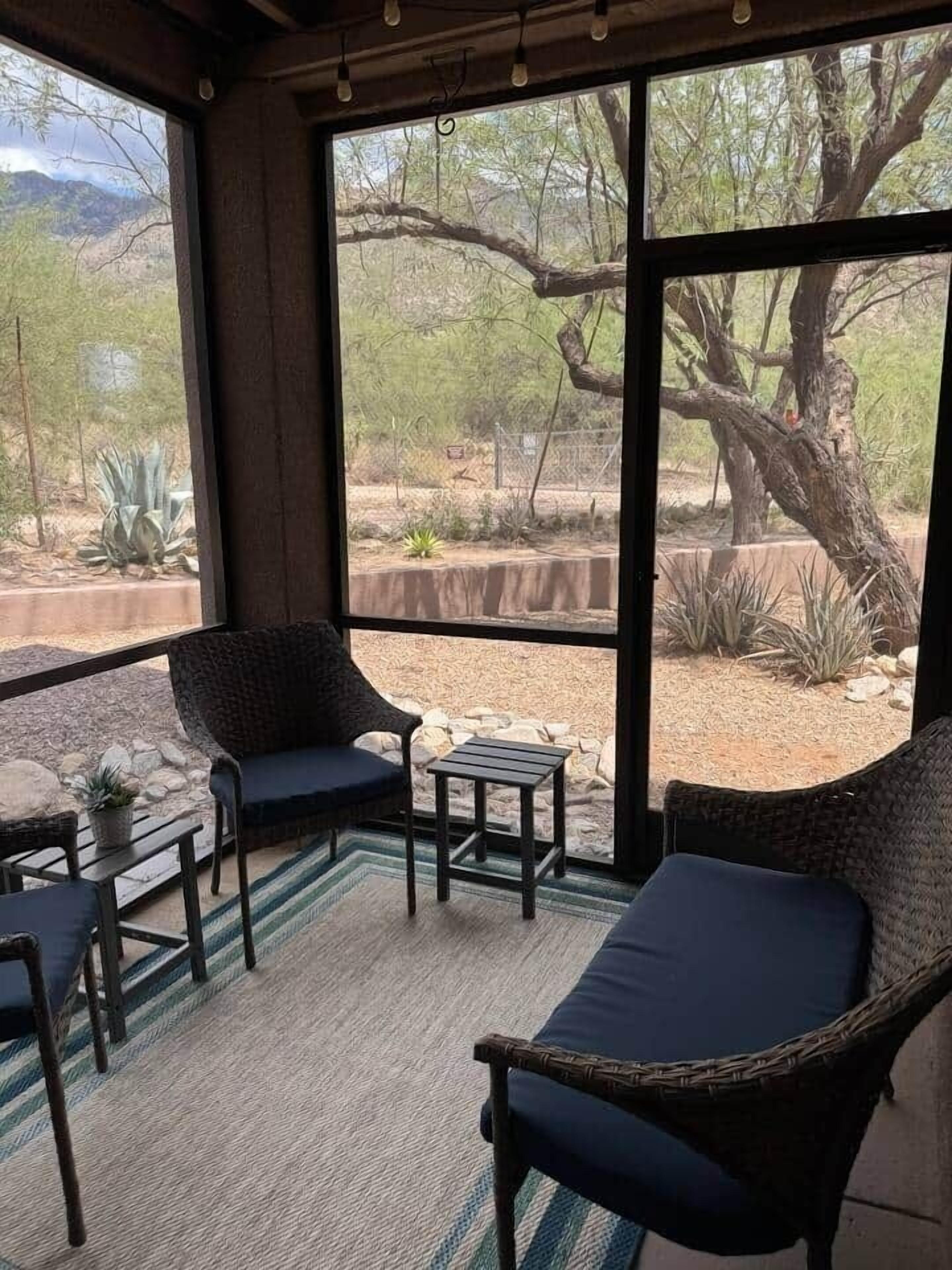 Une véranda meublée de meubles en osier, avec une petite table et une vue sur un paysage désertique, visible à travers de grandes fenêtres.