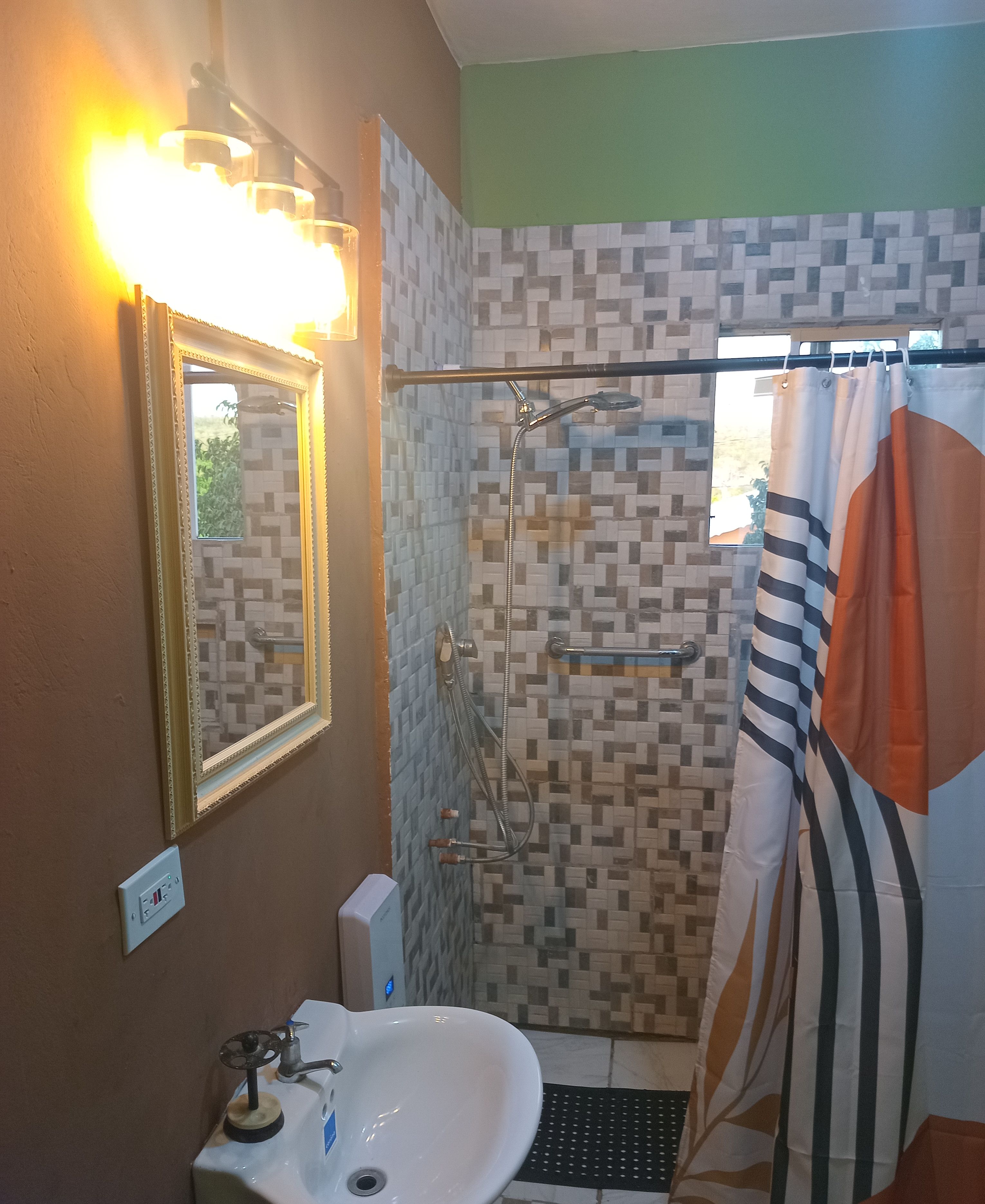 A bathroom with a sink, mirror, shower, and a window with a curtain.