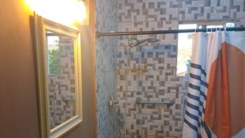 A bathroom with a sink, mirror, shower, and a window with a curtain.