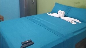 Un letto singolo con copriletto blu, due asciugamani bianchi e un telecomando sul letto.