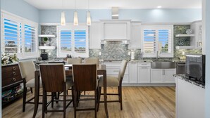 A modern kitchen with white cabinets, a dining area with wooden chairs, and pendant lighting.