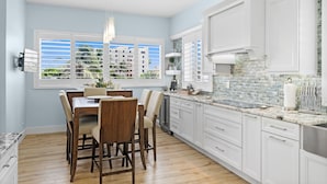 A modern kitchen with white cabinets, a marble countertop, and a large window with blinds.