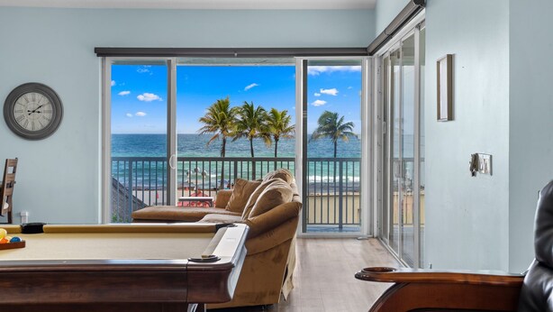 A room with a pool table, a sofa, and a view of the ocean through large sliding glass doors.