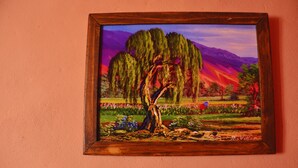 Pintura emoldurada de uma paisagem com árvores, flores e montanhas.