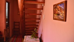 Um corredor estreito com vigas de madeira, uma cadeira, um vaso com planta e um quadro na parede.