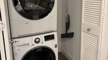 A stacked washer and dryer unit with a broom leaning against the wall.