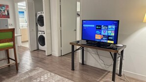 A living room with a flat-screen TV, a wooden chair, a rug, and a washing machine in the background.