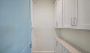 Un pasillo estrecho con armarios blancos y una puerta azul.