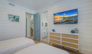 Une chambre avec deux lits, un escalier, un tableau représentant un coucher de soleil et une commode blanche avec des paniers.