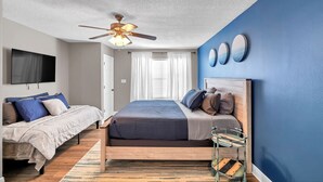 A bedroom with a bed, a desk, a chair, a ceiling fan, and a TV mounted on the wall. - SandSational Staycation Pet Friendly, Fenced Yard, 6min to the Beach (Navarre Beach)