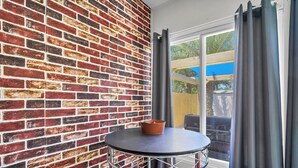 A small room with a brick wall, a round table with a basket, and two red chairs. - SandSational Staycation Pet Friendly, Fenced Yard, 6min to the Beach (Navarre Beach)