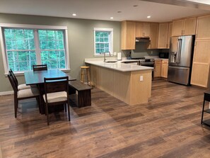 A modern kitchen with wooden cabinets, a central island, and a dining area with a table and chairs.