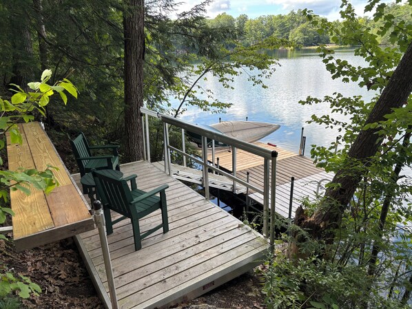 A wooden deck with chairs overlooking a calm lake, surrounded by trees.