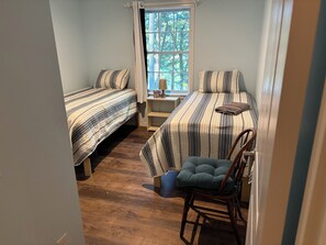 Ein Schlafzimmer mit zwei Betten, einem Sessel und einem Fenster mit Blick auf Bäume.