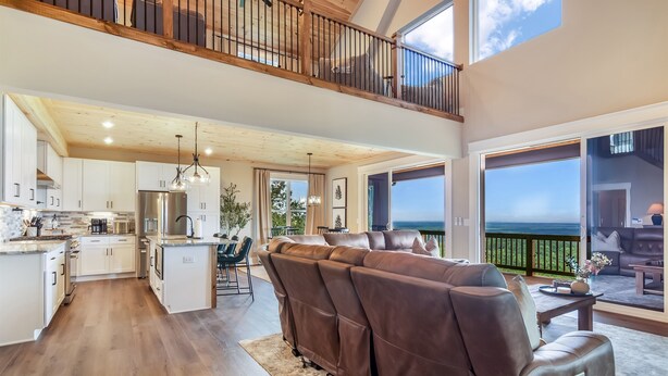 A spacious living area with a large brown sectional sofa, a dining table, and a kitchen with white cabinets and a stainless steel refrigerator. - Stunning Views | Sauna | Hot tub | Bar- 2 Kitchens (Ranger)
