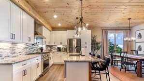 A modern kitchen with white cabinets, a stainless steel refrigerator, and a large island with bar stools. - Stunning Views | Sauna | Hot tub | Bar- 2 Kitchens (Ranger)