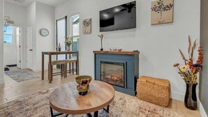 Un salon moderne avec une cheminée, un coin repas avec une table ronde et une cuisine visible au fond.