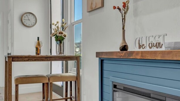Un salon moderne avec une cheminée bleue, une table en bois avec deux chaises, un vase de fleurs et une horloge murale.