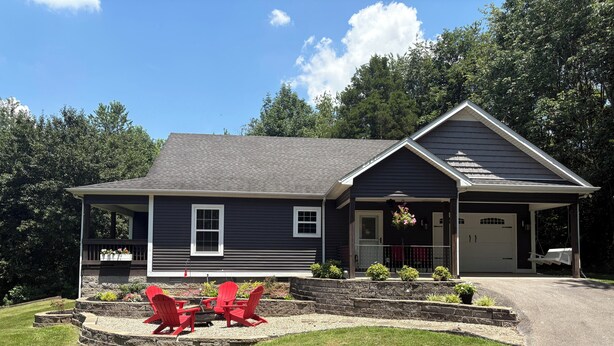 A two-story house with a covered porch, a garage, and a landscaped front yard with red Adirondack chairs and a fire pit. - Cottage at Sunnyside/Private/5 Wooded Acres/Garage (Bowling Green)
