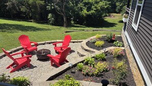 A patio with red Adirondack chairs, a fire pit, and a garden with various plants and flowers. - Cottage at Sunnyside/Private/5 Wooded Acres/Garage (Bowling Green)