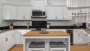 A modern kitchen with white cabinets, a wooden island with two stools, a built-in oven, and a microwave.