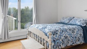 A bedroom with a large window, a bed with a floral bedspread, and a wooden bench.