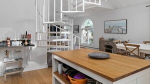 A modern kitchen with white cabinetry, a wooden island, and a white spiral staircase.