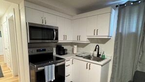 Une cuisine de taille réduite avec des meubles blancs, un four à micro-ondes encastré, une cuisinière et un évier.