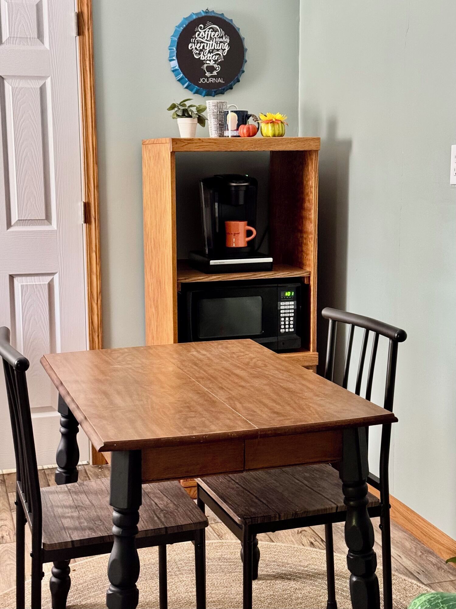 A dining table with chairs, a coffee maker, a microwave, and a decorative plate on a shelf.