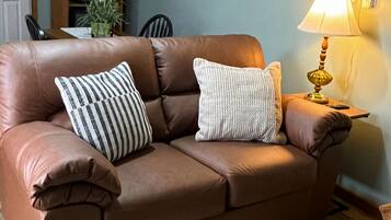 A brown leather sofa with two pillows, a small rug, and a table lamp.