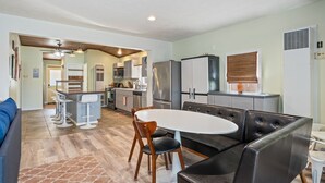Een moderne keuken met een centraal eiland, een eetgedeelte met een ronde tafel en lederen stoelen, en een woonkamer met een bank en een salontafel.