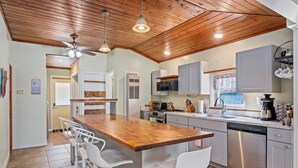 Een moderne keuken met een houten plafond, roestvrijstalen apparatuur en een centraal eiland met barkrukken.