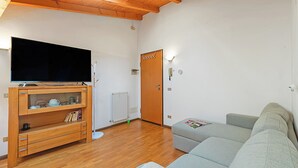 A living room with a wooden TV stand, grey sofa, and wooden ceiling beams. - Skylight, Riva del Garda, Italy (Riva del Garda)