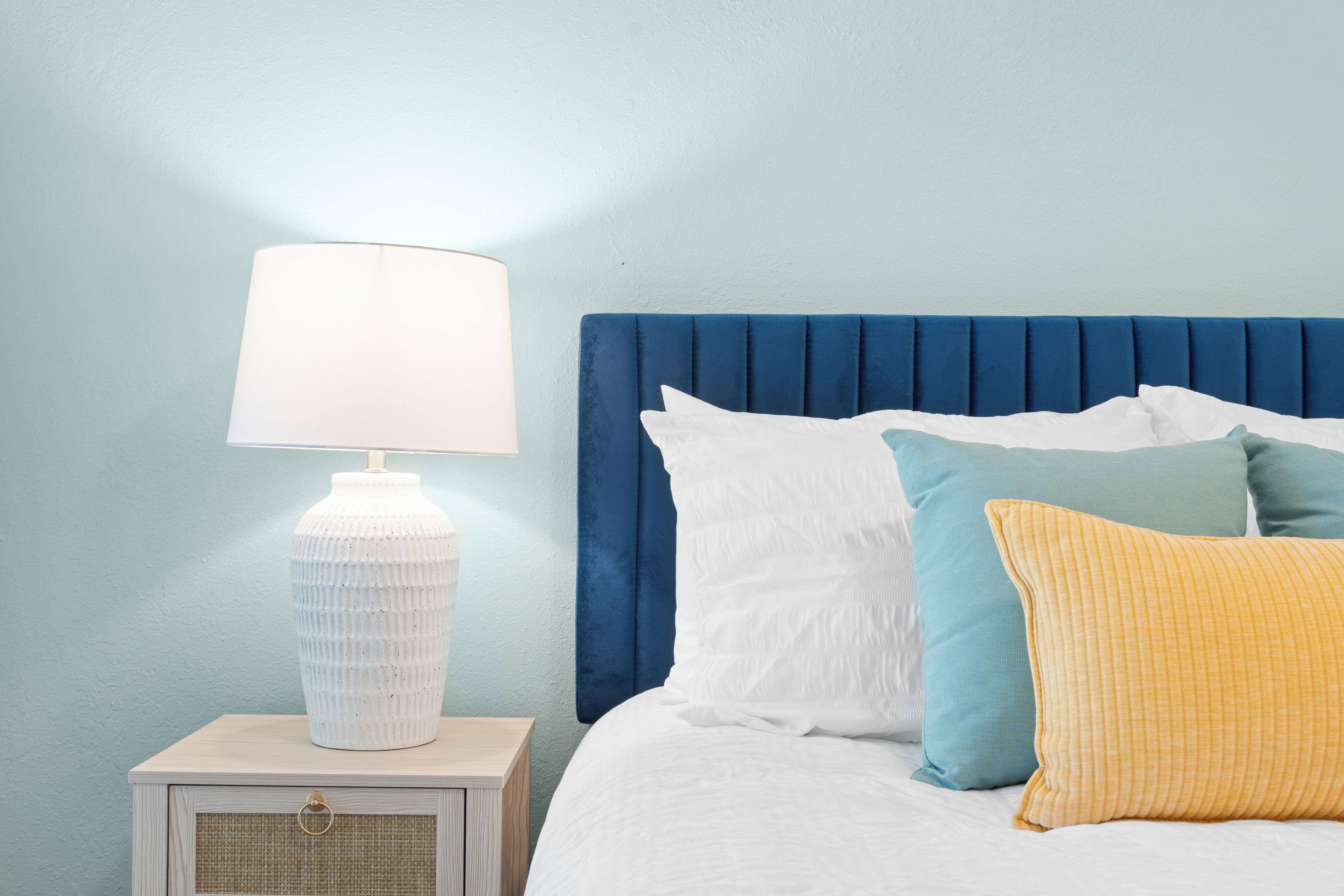 A bed with a blue headboard, white bedding, and multiple pillows in various colors.
