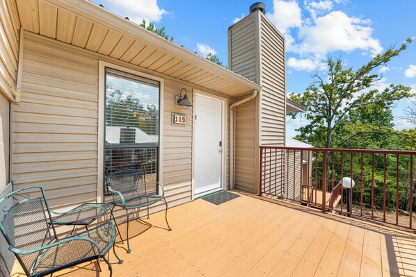 A covered deck with metal chairs, a white garage door, and a red railing.