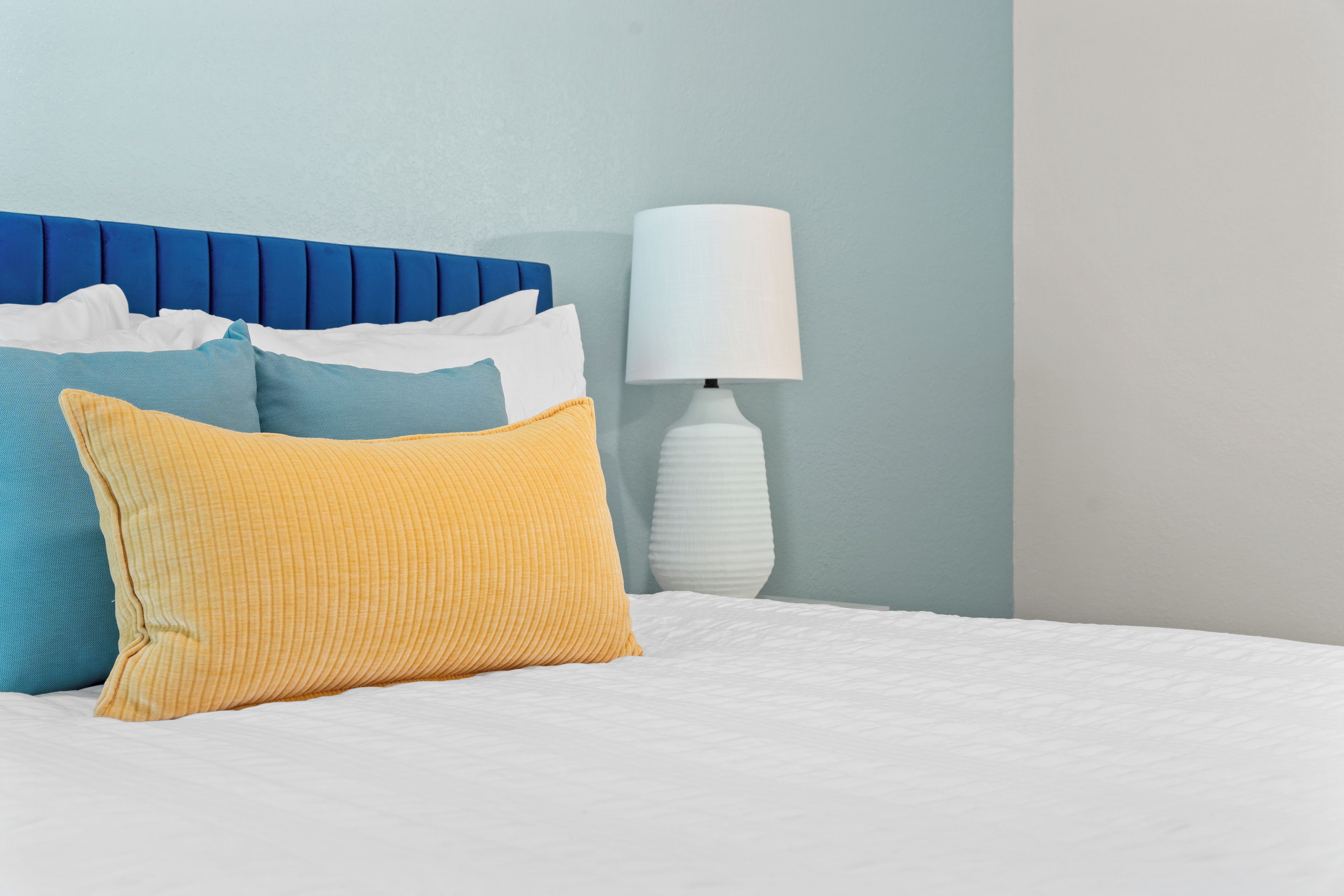 Ein Bett mit weißer Bettwäsche, einem blauen Kopfteil und mehreren Kissen in verschiedenen Farben.