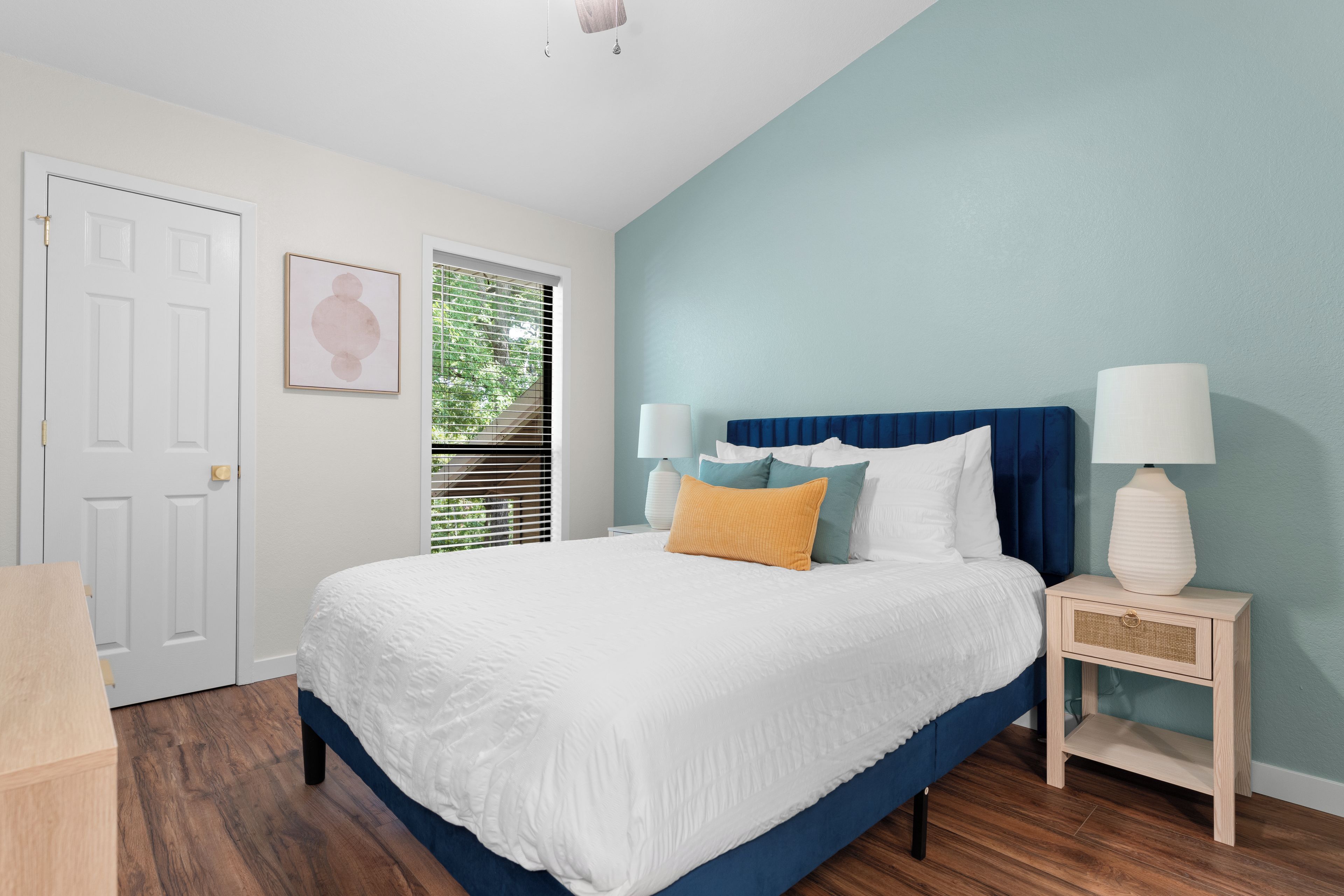 A bedroom with a bed, bedside tables, a door, and a window with blinds.