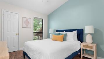 A bedroom with a bed, bedside tables, a door, and a window with blinds.