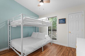 A bunk bed in a room with wooden flooring, a ceiling fan, and a window with blinds.