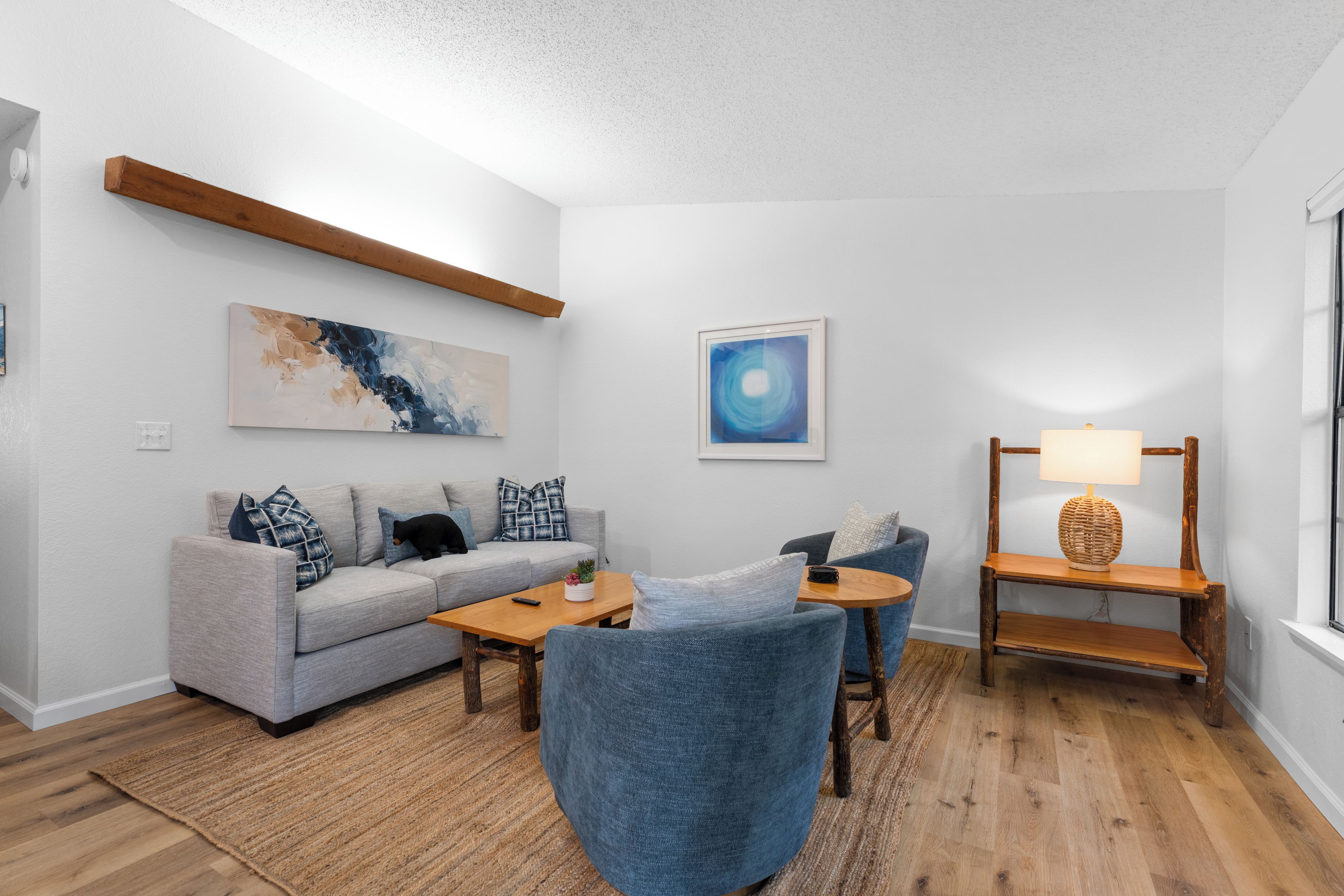 A modern living room with a grey sofa, blue armchairs, a wooden coffee table, and a wooden side table with a lamp.
