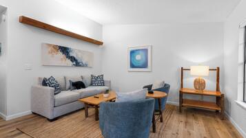 A modern living room with a grey sofa, blue armchairs, a wooden coffee table, and a wooden side table with a lamp.