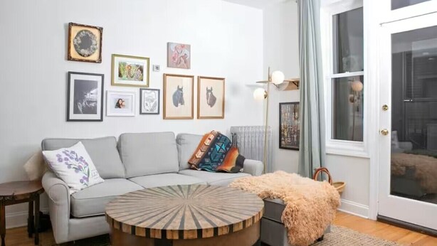 Una sala de estar con un sofá gris, una mesa de centro redonda y cuadros en la pared.