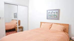 Un dormitorio con una cama, cabecera de madera, una mesita de noche pequeña, un cesto de basura y un cuadro enmarcado en la pared.
